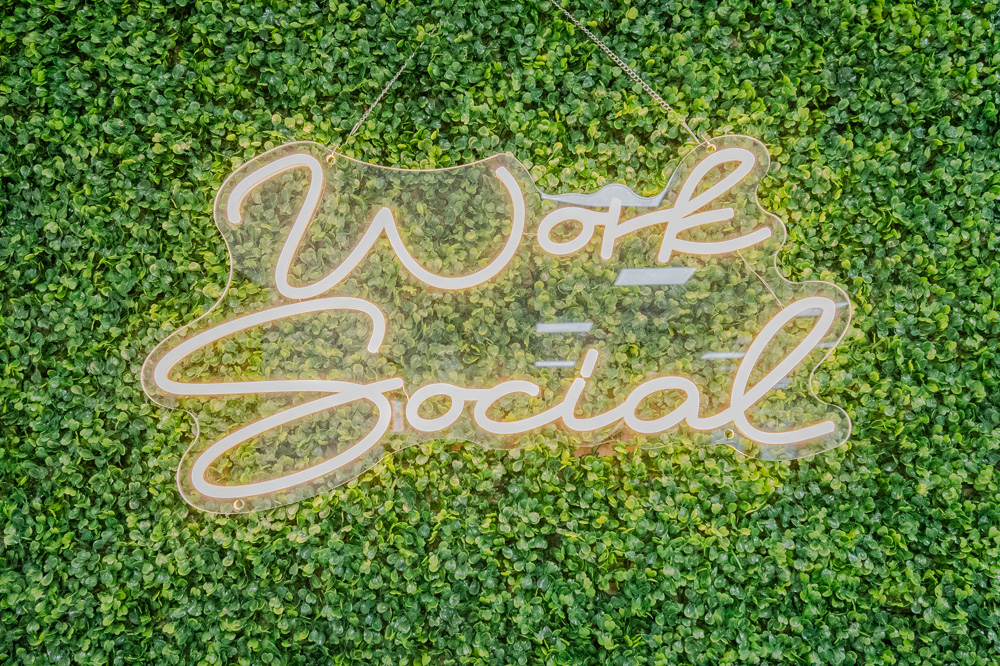 Work Social neon sign on a green plant wall